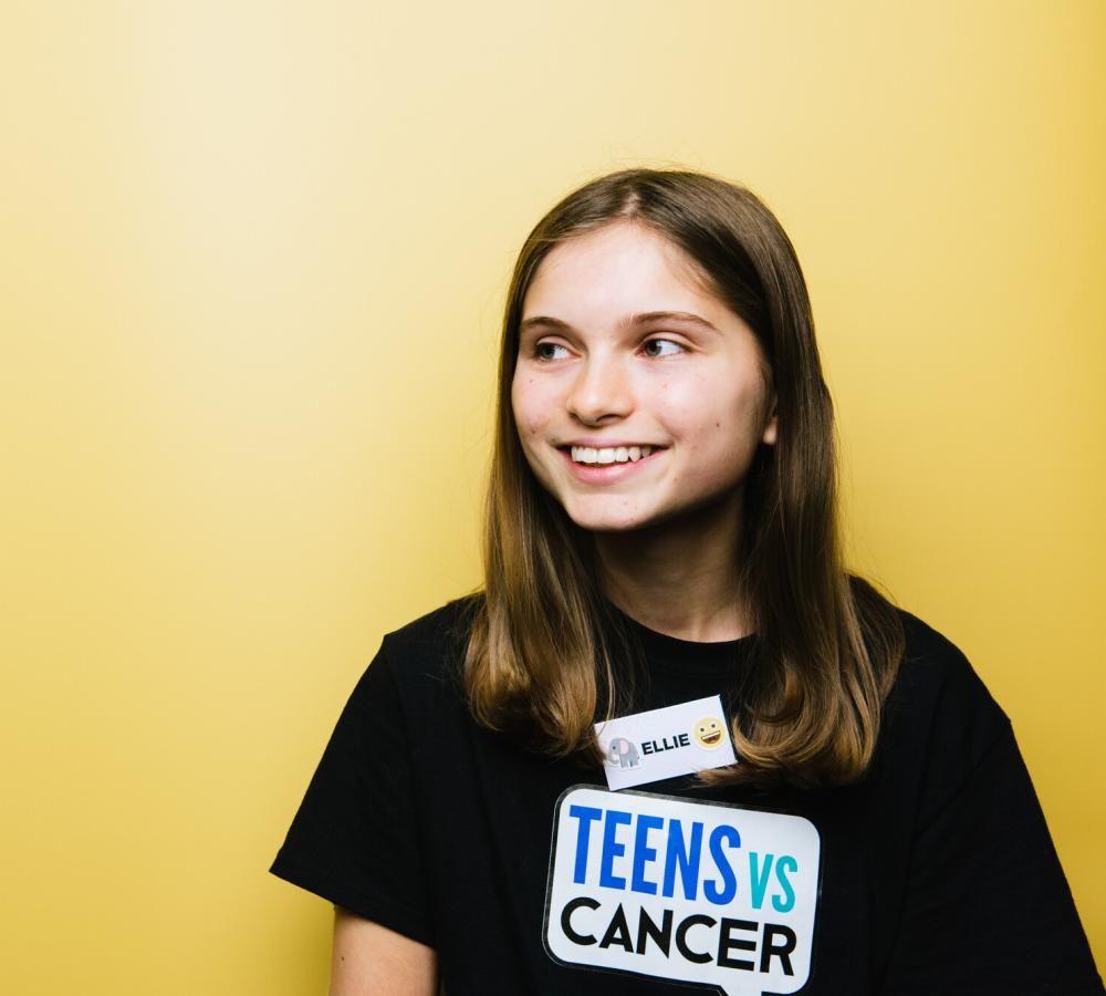 A young person with cancer stood in front of a yellow backdrop