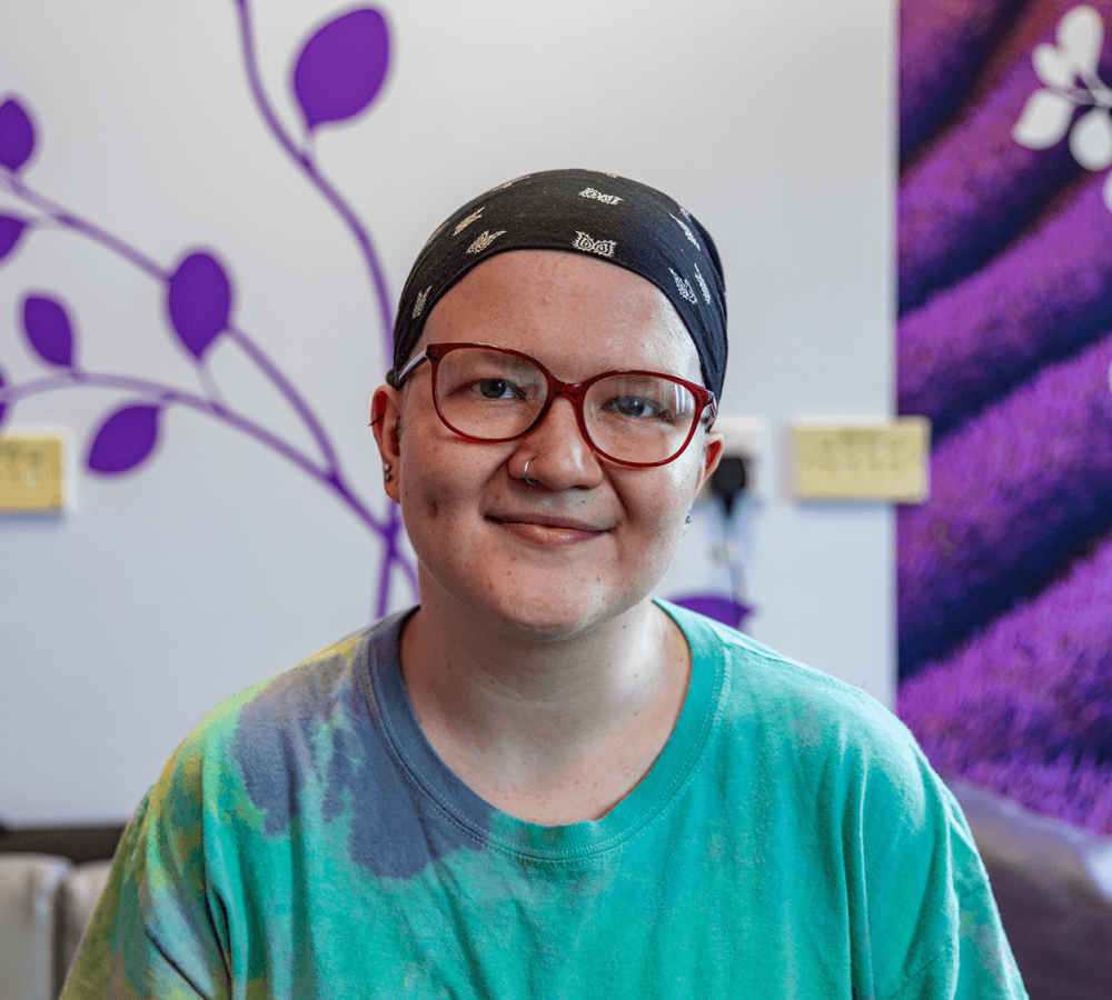 Young person with cancer in a Teenage Cancer Trust ward, wearing a head scarf and looking happy.