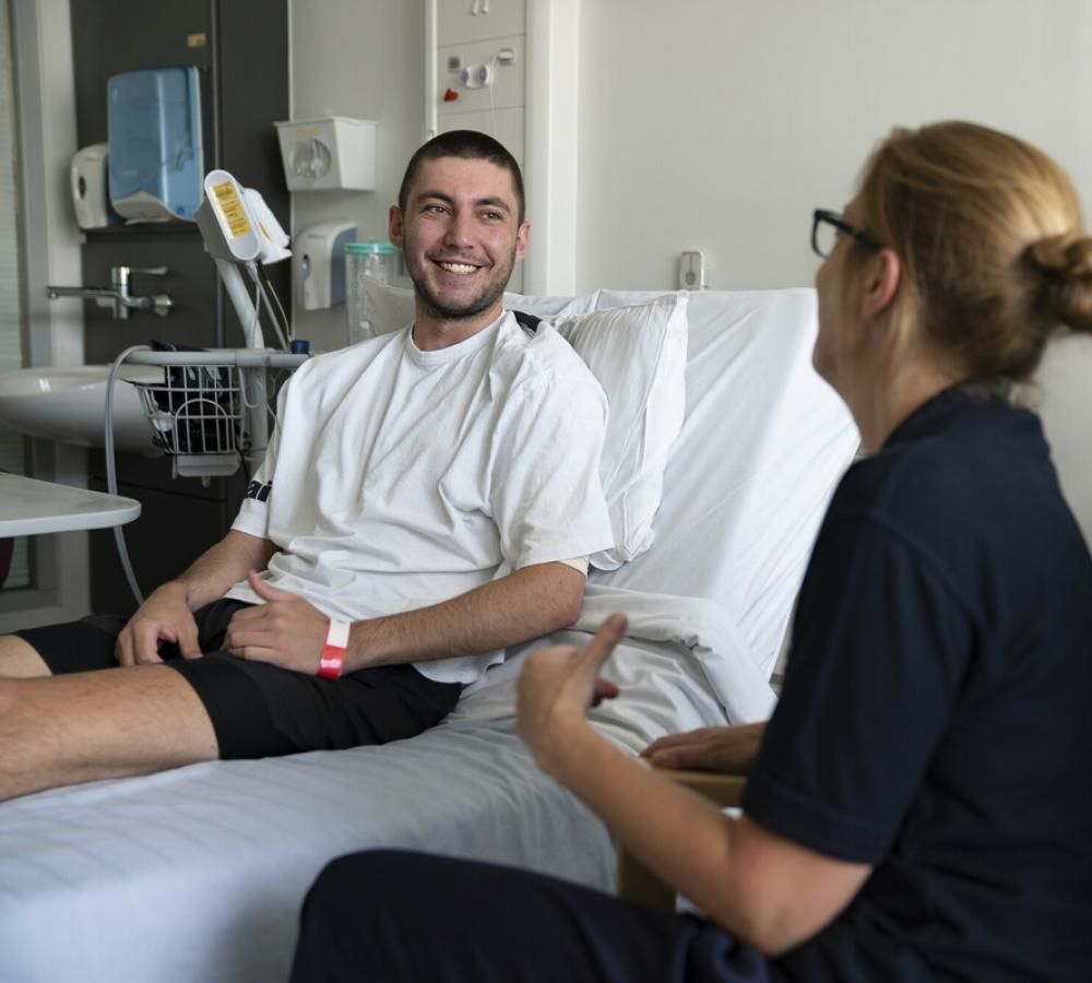 Young person on hospital bed talking with Teenage Cancer Trust nurse