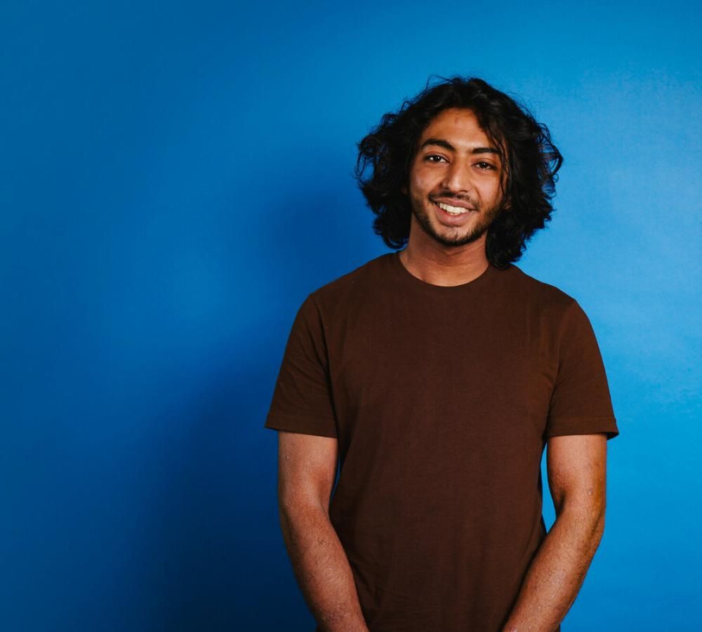 Zaki from Teenage Cancer Trust's Youth Advisory Group against a blue background smiling