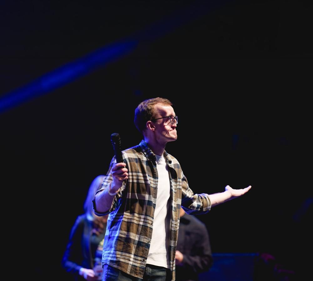 A young man wearing a plaid shirt stands on stage at the Royal Albert Hall