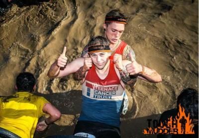 Two young people during tough mudder, dragging one and other through watery mud
