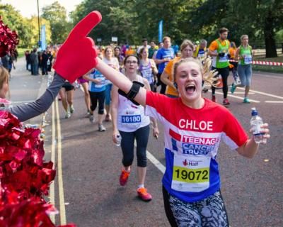 A young person running past the Teenage Cancer Trust cheer squad at the Royal Parks Half Marathon