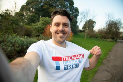 A fundraiser outdoors wearing a white t-shirt with the Teenage Cancer Trust logo on its front