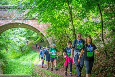 A group of walkers taking on the Cotswold Way Challenge walking beneath a bridge on a country path
