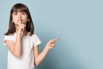 A little girl making a shush signal by holding finger on lips