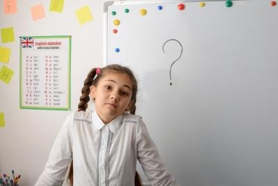 A schoolgirl holding a quiz standing in front of a whiteboard with a question mark on it