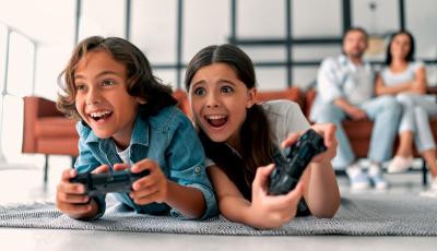 A young boy and a young girl playing videogames while their parents watch on the sofa