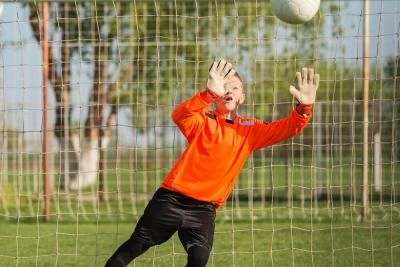 A young goalkeeper trying to save a football which is going towards his goal