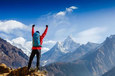 A climber who is celebrating with their arms raised after climbing a mountain to raise money for Teenage Cancer Trust