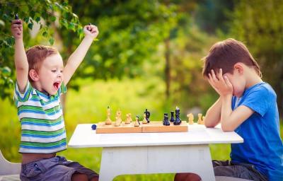 One young boy has his hands in the air and the other young boy has his head in his hands after a game of chess