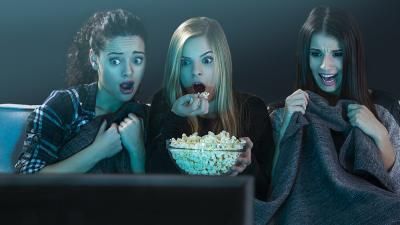 Three women watching a scary movie as part of a Halloween movie marathon to raise money for Teenage Cancer Trust