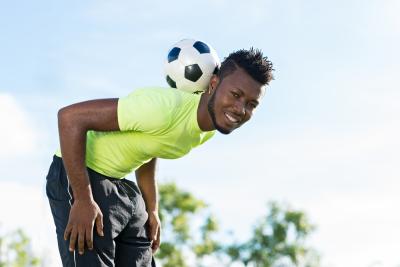 A man smiling balancing a football behind his head