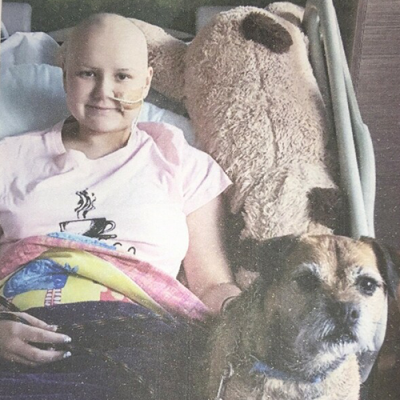 Young person with cancer laying in a hospital bed with her pet dog.