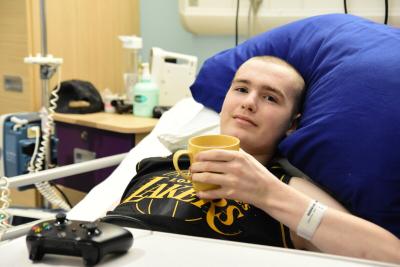 Aidan, a young person with cancer, laying in a Teenage Cancer Trust ward about to start gaming for charity