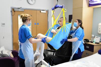 Aidan, a young person with cancer, being moved by Teenage Cancer Trust nurses in a medical swing