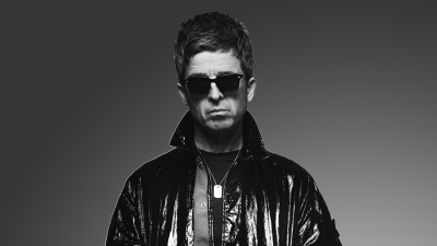 Noel Gallagher, black and white portrait in a black jacket and dark glasses.