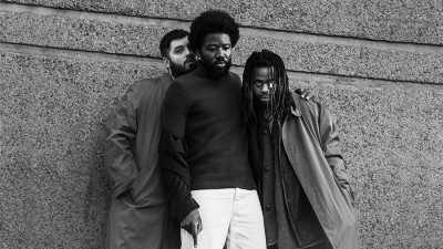 A music group, Young Fathers, standing against a concreate wall