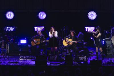 Eddie Vedder, wearing a cowboy hat, and his band onstage. Vedder's daughter is singing at the mic wearing a black and white outfit. 