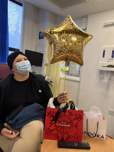 Kirah holds a golden star shaped balloon with Congratulations message. She is surrounded by gift bags and though she is wearing a face mask you can tell she is smiling.