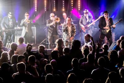 An eight-piece band performs on stage to a crowd at Teenage Cancer Trust event