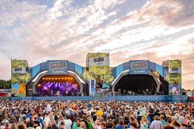 A large crowd watching a band perform on stage at CarFest as the sun sets