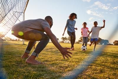 A family playing football, a boy is trying to score a goal against a man