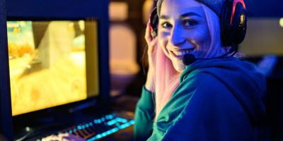 A smiling person wearing a hoodie and gaming headset playing a PC game