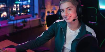 A smiling person sitting in a gaming chair wearing a headset with their hand on a computer mouse
