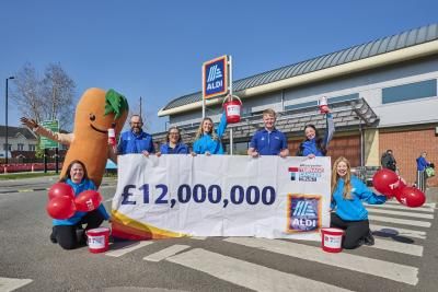 Aldi employees celebrating and holding a huge teenage cancer trust branded banner, displaying £12 million pounds