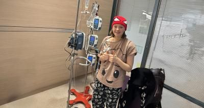 Young person with cancer, attached to a medical drip, undergoing treatment. They are in their pyjamas, wearing a red bandana on their head.