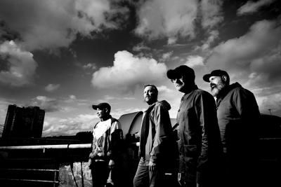 The band Mogwai standing outside with a cloudy sky in the background
