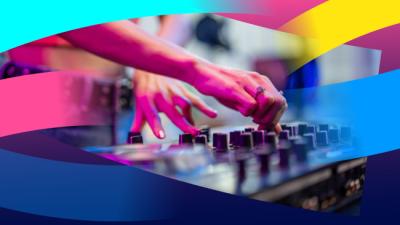 A person focused on mixing music using a DJ mixer, surrounded by colourful lights and equipment