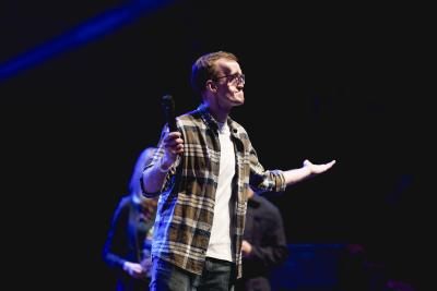 A young man wearing a plaid shirt stands on stage