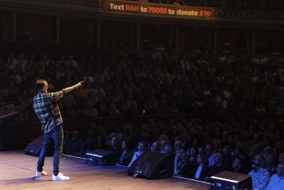 A young man wearing a plaid shirt stands on stage at the Royal Albert Hall