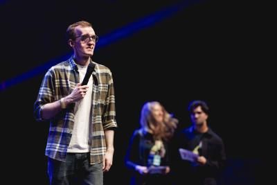 A young man wearing a plaid shirt stands on stage at the Royal Albert Hall