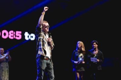 A young man wearing a plaid shirt stands on stage at the Royal Albert Hall