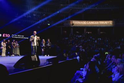 A young man wearing a plaid shirt stands on stage at the Royal Albert Hall