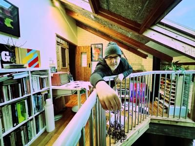 A man with a beanie hat and great beard leans over a staircare. In the background are lots of 12" vinyl records