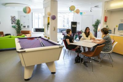 Young people and staff sit chatting at a table at the brightly decorated Teenage Cancer Trust unit in Bristol