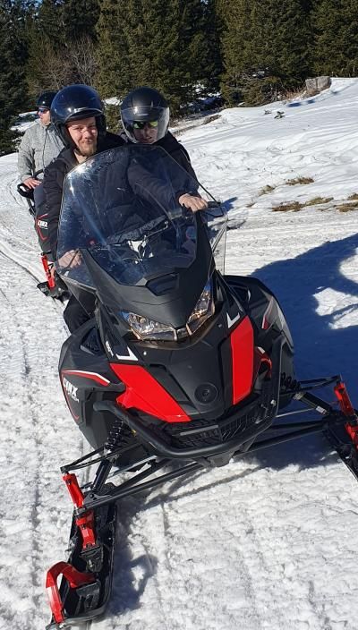 A man in a helmet sits on a jet ski with snowy grounds and forest-like background