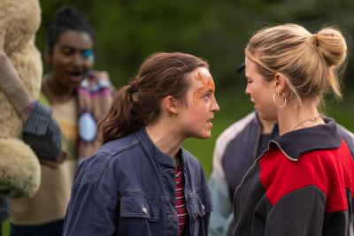 A young woman in a denim jacket squares up to a blonde girl with a red and navy jacket