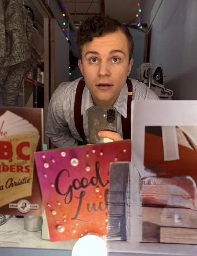 A young man with brown hair takes a selfie in a mirror surrounded by 'good luck' cards