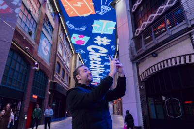 Jason Manford taking photos at Printworks exhibition with ceiling digital screen as backdrop
