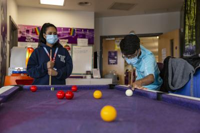 Young person and youth worker playing pool in brightly coloured social area on Teenage Cancer Trust unit