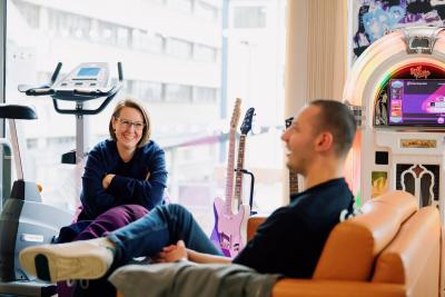 Young man and Teenage Cancer Trust youth worker smiling and chatting while sat in bright colourful social area on Teenage Cancer Trust unit