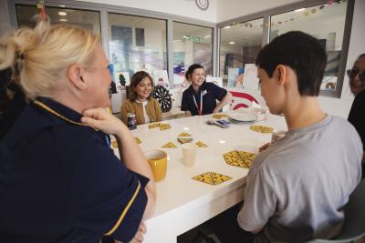 Young people, nurse and youth worker sat round a table smiling and playing a card game on the Teenage Cancer Trust unit