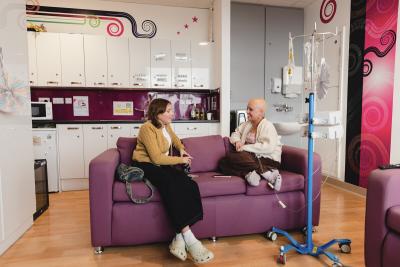 Two young women sat on a sofa smiling and chatting on the Teenage Cancer Trust unit