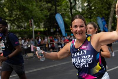 A young woman runs past the Teenage Cancer Trust cheer point, smiling!