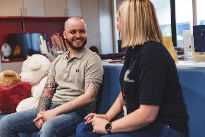Young person and youth worker sitting on sofa chatting in Teenage Cancer Trust unit